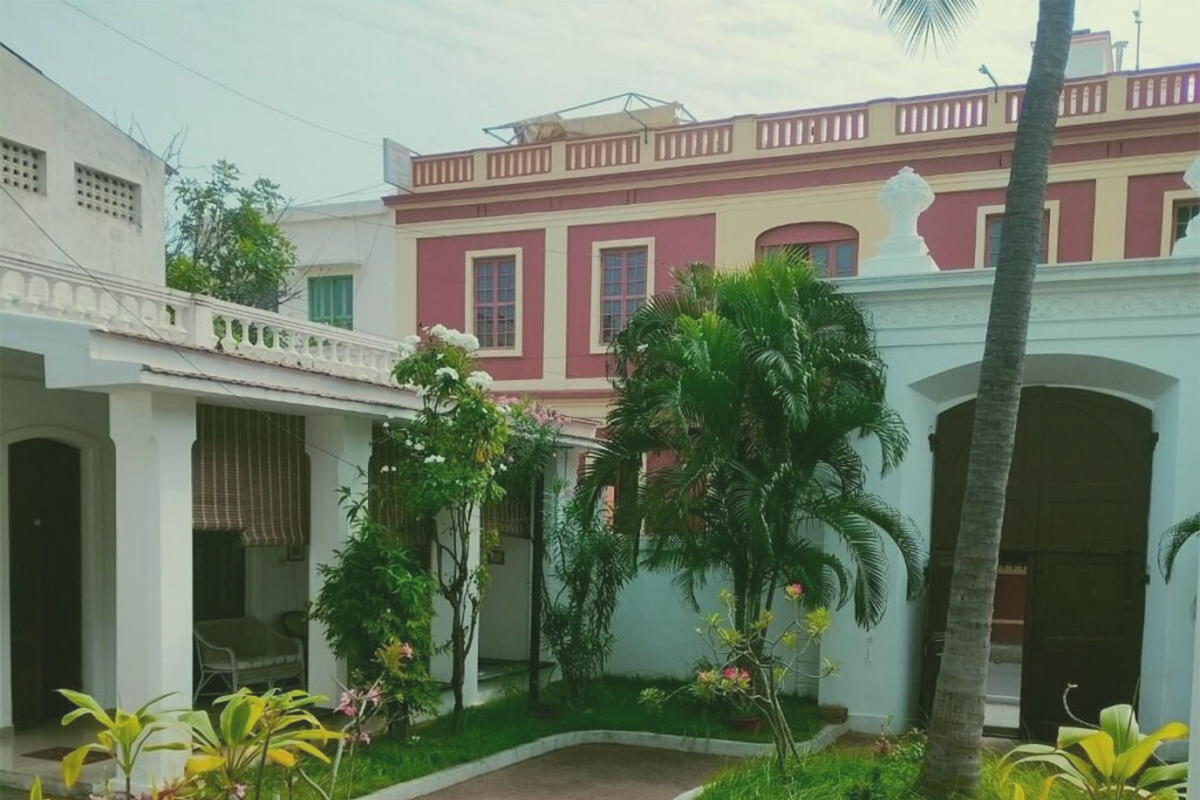 The exterior of the 18th-century French colonial building housing the Cluny Embroidery Centre in Pondicherry, featuring a yellow facade, white trim, and a terracotta tiled roof with a long covered veranda.