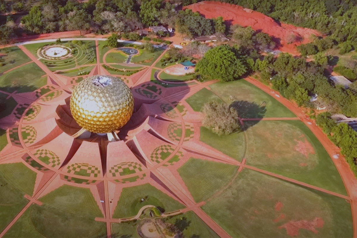 A stunning aerial photograph of the Matrimandir, a giant golden globe structure, situated at the heart of Auroville and surrounded by the intricately designed Peace Gardens and lush greenery.
