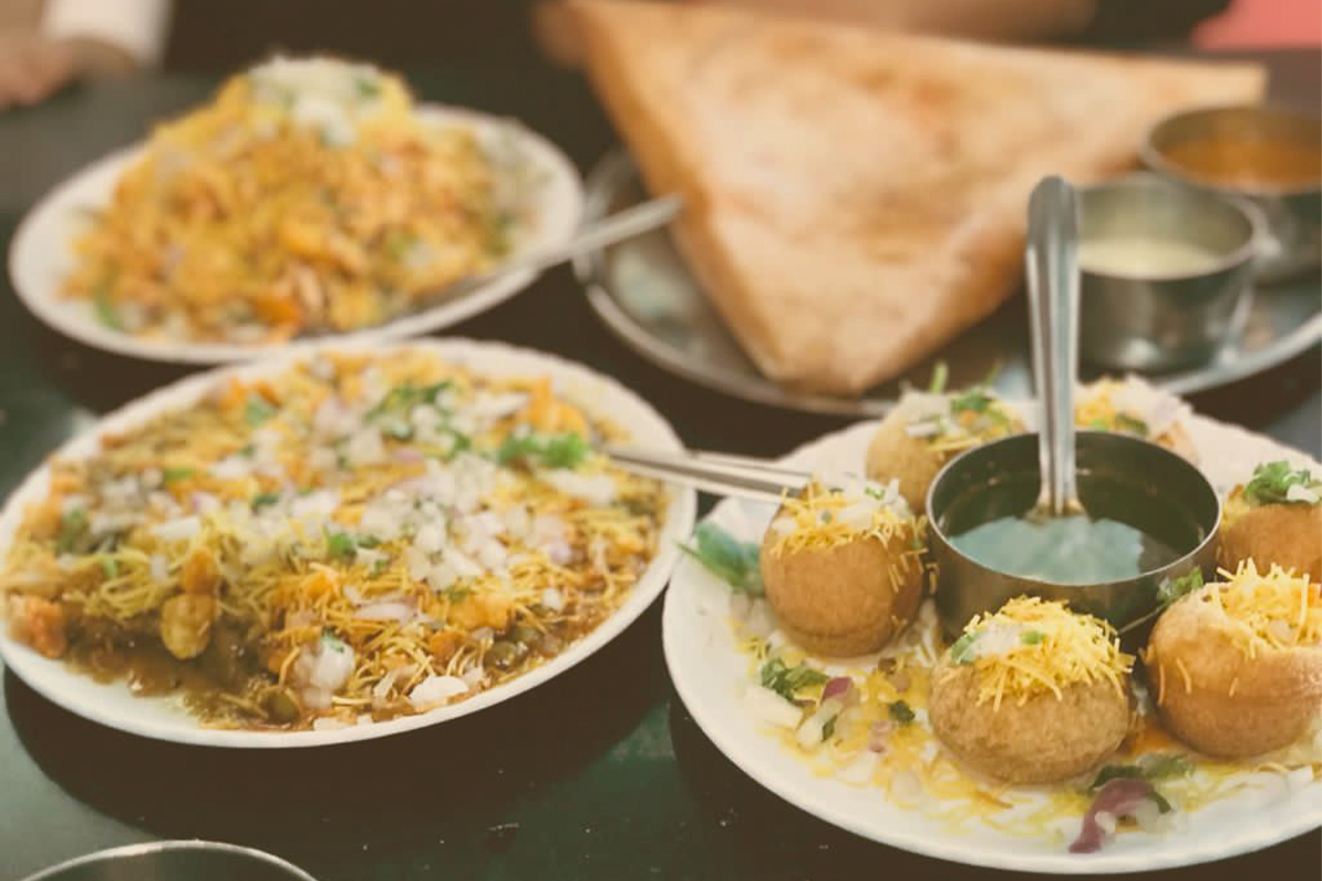 A lively street food cart with vendors and customers on the seaside promenade in Pondicherry, India, with the Bay of Bengal in the background during evening.