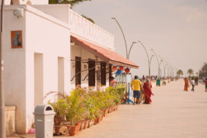 Exterior view of Le Café, a popular French-style cafe located on the beach promenade in Pondicherry, India, with customers and its sign visible.